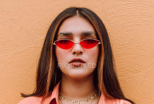 Portrait de femme charismatique avec des lunettes de soleil tendance contre le mur orange regardant la caméra — Photo de stock
