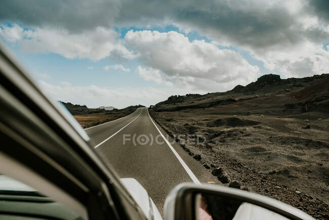 Veículo que conduz em estrada de asfalto através de terreno vulcânico árido no dia nublado na natureza de Fuerteventura, Espanha — Fotografia de Stock