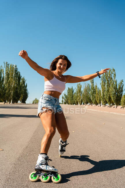 Вид збоку підходить весела жінка в роликових лопатях, що показує трюк на дорозі в місті влітку — стокове фото