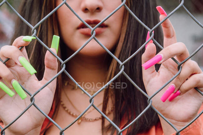 Crop view of stylish female with bright long manicure standing near metal fence — Stock Photo