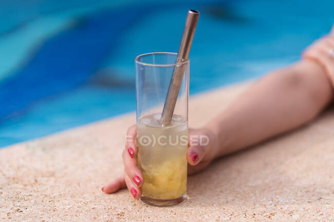 Зверху врожаю самка зі склянкою освіжаючого коктейлю з кубиками льоду і нульовою соломою металу, розміщеною біля басейну в сонячний день влітку — стокове фото