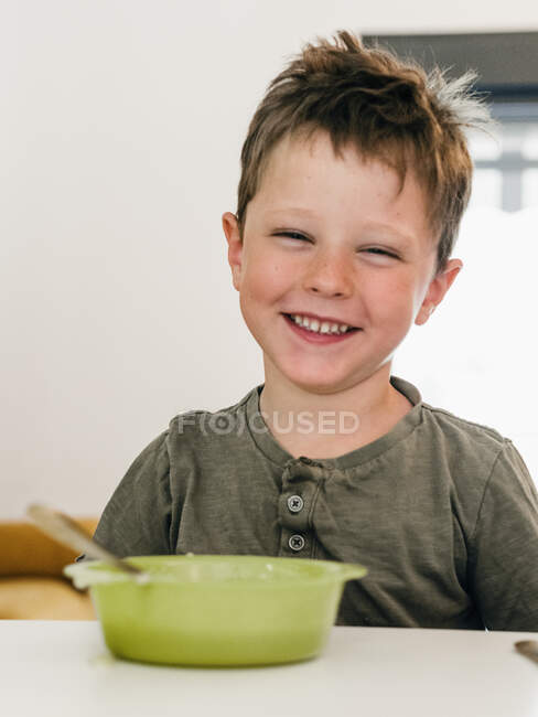 Retrato de menino alegre adorável sentado à mesa na hora do almoço em casa sorrindo para a câmera — Fotografia de Stock