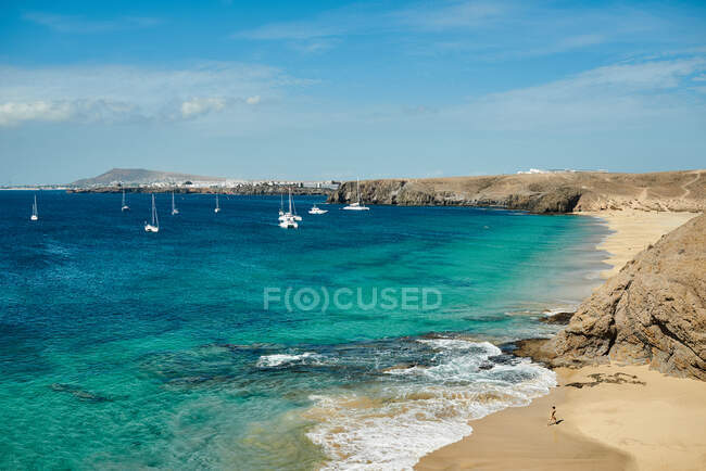 Praia com veleiros ao fundo em um mar azul-turquesa sob um céu com nuvens no dia ensolarado de verão em Fuerteventura, Espanha — Fotografia de Stock