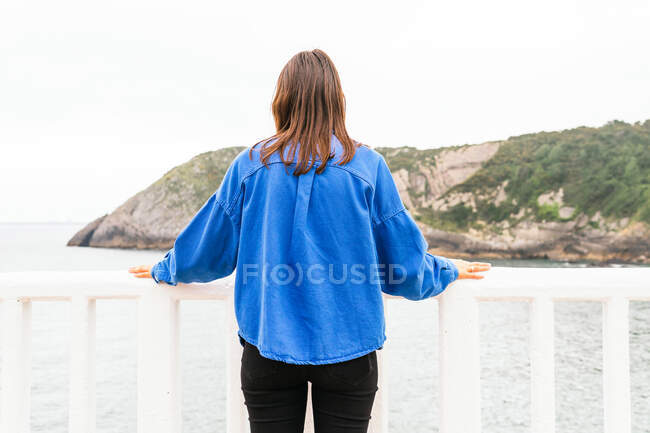 Visão traseira da fêmea irreconhecível em pé perto de trilhos no calçadão e admirando a vista do mar — Fotografia de Stock