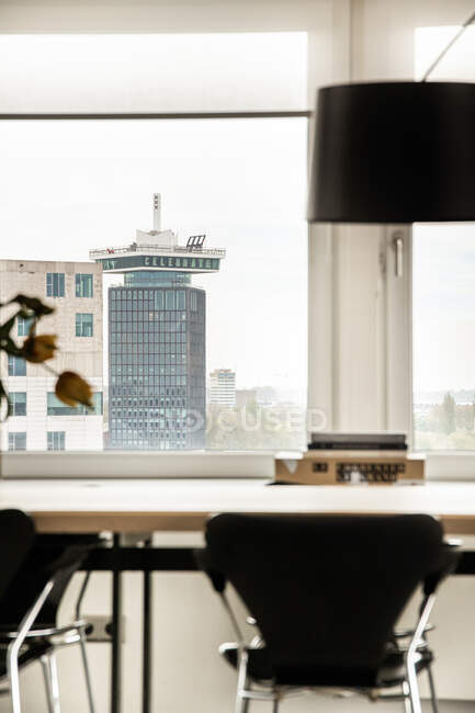 Interieur der modernen Wohnung mit Tisch und Stühlen in der Nähe von Panoramafenster mit Blick auf die Stadtlandschaft mit zeitgenössischer Architektur bei Tageslicht — Stockfoto