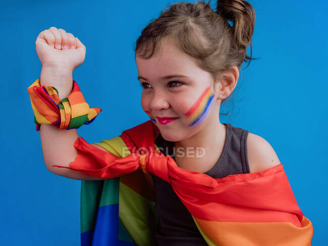 Cute glad child with multicolored bandage on neck and wrist standing against blue background and looking away — Stock Photo