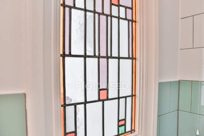 Фрагмент интерьера с красочным мозаичным окном и черепичной стеной при дневном свете в доме — стоковое фото