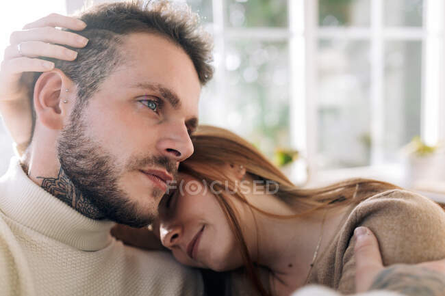 Lächelnde junge Frau streichelt Haare tätowierter männlicher Geliebter, während sie an sonnigen Tagen im Haus ruht — Stockfoto