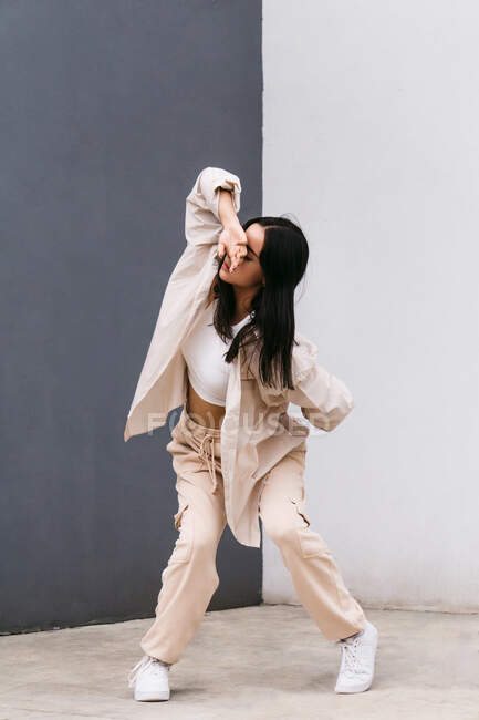 Bailarina femenina creativa de cuerpo entero en ropa blanca bailando en la calle de la ciudad durante la actuación tocando la cabeza con la mano - foto de stock
