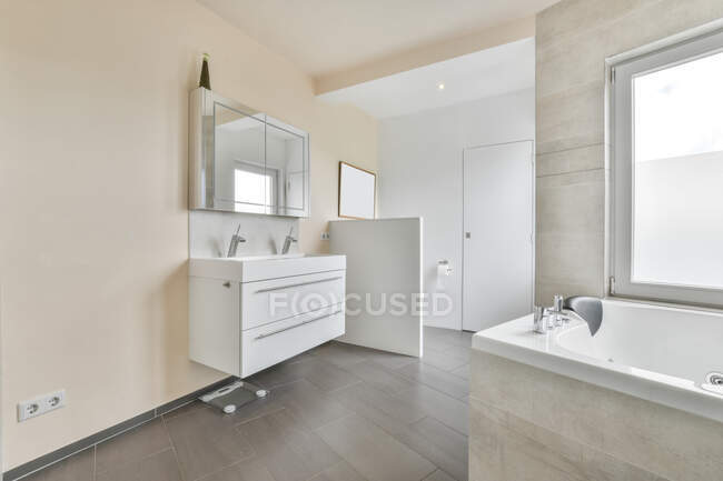 Interior do banheiro espaçoso com paredes bege claro decorado com lavatório duplo sob espelho e banheira no apartamento moderno — Fotografia de Stock