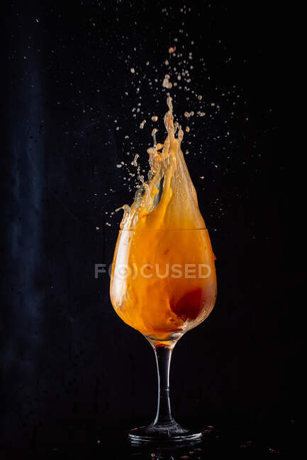 Cold alcohol orange drink splashing out of glass goblet on black background in studio — Stock Photo