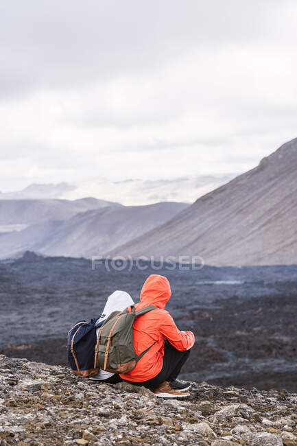 Blick zurück auf anonyme Reisende in Oberbekleidung, die Lava des Fagradalsfjalls von einem Berg unter wolkenverhangenem Himmel in Island betrachten — Stockfoto