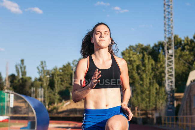 Зосереджений на професійному жіночому атлеті, який біжить на стадіоні в сонячний день влітку. — стокове фото