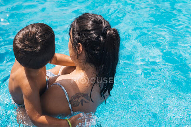Vista superior da mãe irreconhecível com o filho em pé na piscina no dia ensolarado de verão — Fotografia de Stock