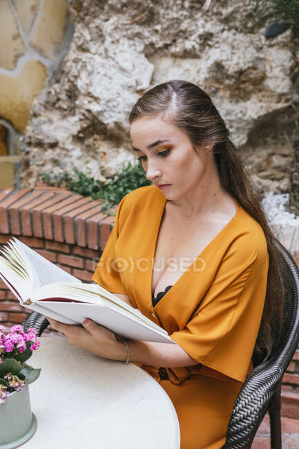 Lectura femenina tierna serena libro interesante mientras se sienta a la mesa en la terraza de verano de la casa - foto de stock