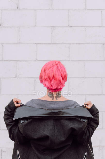 Вид сзади Неузнаваемая самка с окрашенными волосами и татуировкой крыльев на шее, стоящая возле белой стены — стоковое фото