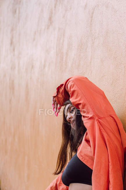 Femme sereine en tenue moderne avec une manucure longue et brillante et le visage recouvert de cheveux levant les mains sur fond orange — Photo de stock
