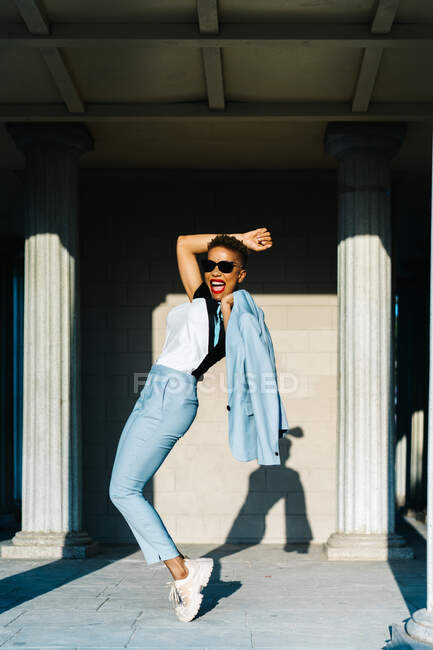 Side view of excited ethnic female in stylish wear and sunglasses having fun on urban pavement in sunlight — Stock Photo