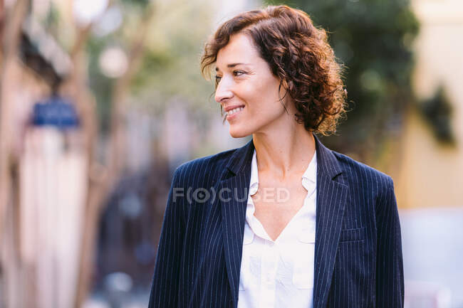 Mulher positiva em roupas elegantes andando na rua sorrindo olhando para longe — Fotografia de Stock
