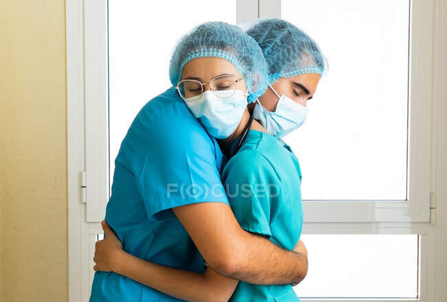 Vista laterale di medici in uniforme e maschere protettive abbracciano mentre in piedi in ospedale — Foto stock
