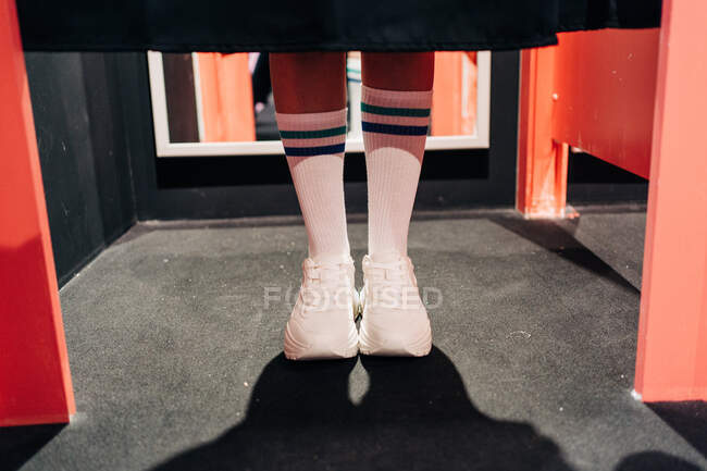 Cortar fêmea elegante irreconhecível no joelho meias altas e tênis brancos em pé atrás da cortina no armário de mudança — Fotografia de Stock