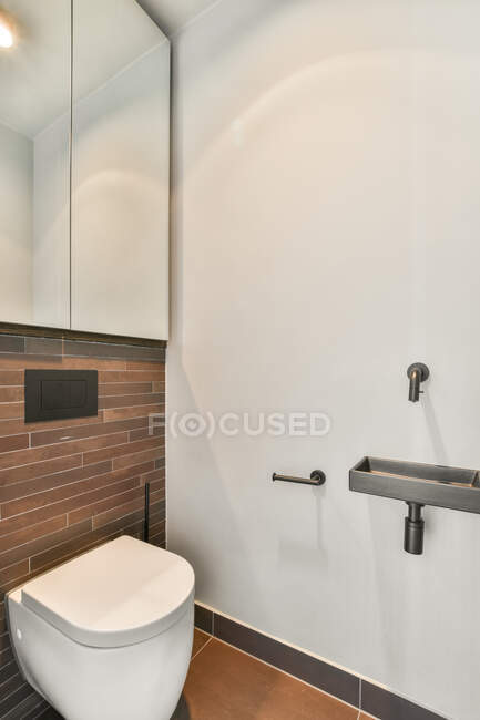 Интерьер современного туалета с белым туалетом расположен возле кирпичной стены с зеркалом и раковиной — стоковое фото
