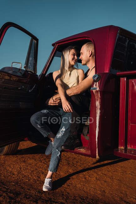 Young couple in love sitting in red vintage pickup in sunset in summer — Stock Photo