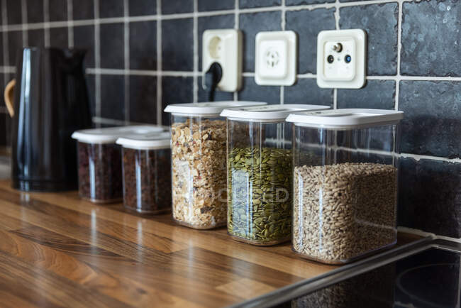 Plastic containers with muesli and sunflower and pumpkin seeds placed near coffee beans and electric kettle on counter in kitchen — Stock Photo
