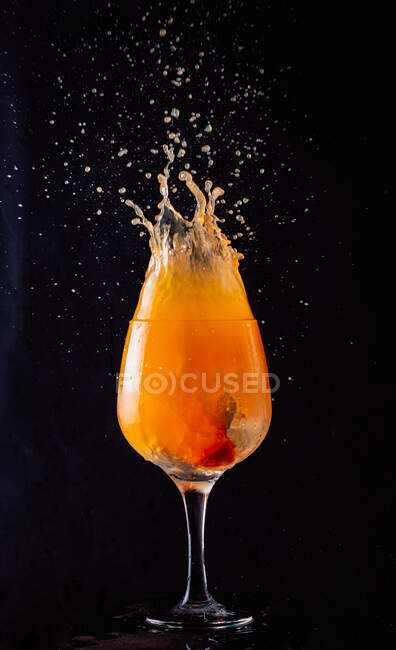 Boisson froide à l'alcool orange éclaboussant de gobelet de verre sur fond noir en studio — Photo de stock