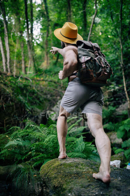 Von unten ein hirnloser Mann mit Rucksack und Hut, der im felsigen Wald steht und wegschaut — Stockfoto