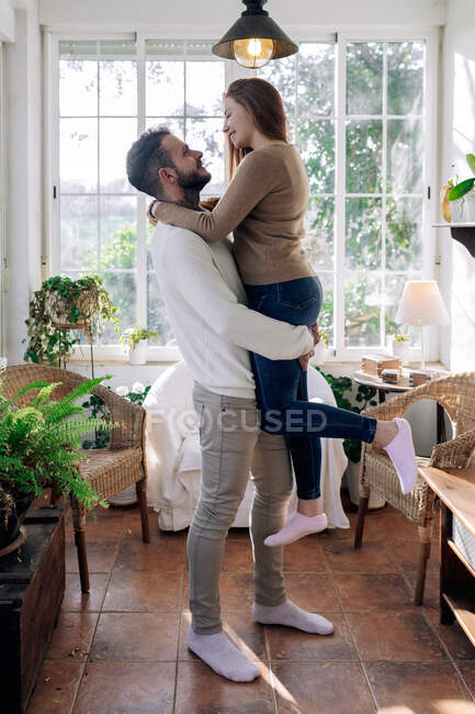 Sorridente donna cavalcando sul fidanzato mentre si guardava l'un l'altro contro le finestre a casa — Foto stock