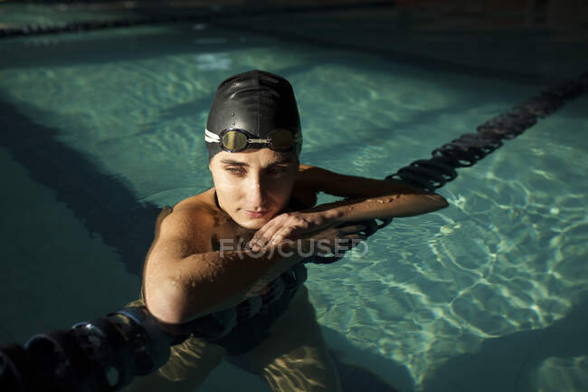 Jeune belle femme à l'intérieur de la piscine intérieure, portant un maillot de bain noir et tenant la péniche de natation — Photo de stock