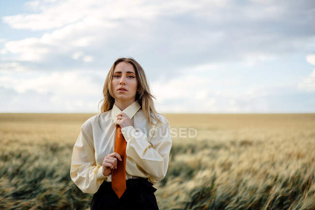 Giovane donna consapevole in abbigliamento formale con cravatta guardando la fotocamera tra punte in campagna — Foto stock