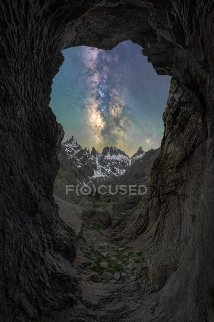Через печеру вид на засніжені гори та зоряне небо з галактикою та міжзоряним газом на заході сонця — стокове фото