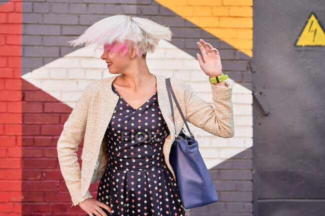 Carefree alternative female throwing dyed short hair against colorful wall in urban area — Stock Photo
