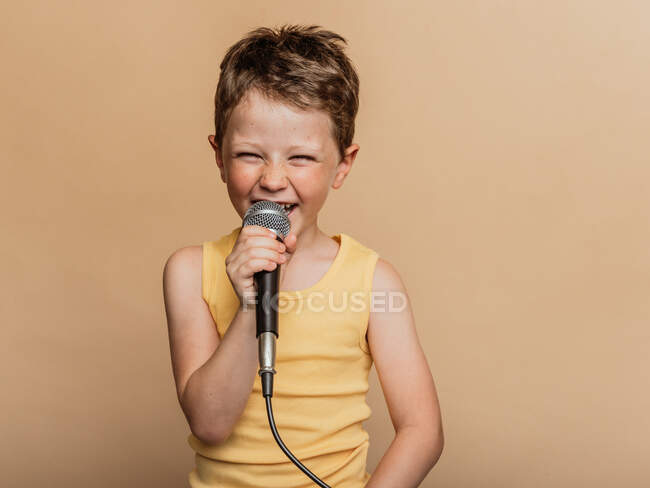 Cool child in singing in modern mic on brown background in studio — Stock Photo