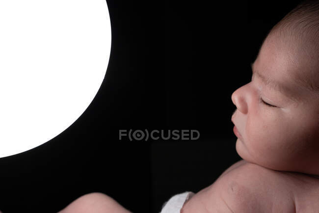 Side view of tender infant sleeping on bed and touching glowing night light lamp in dark room — Stock Photo