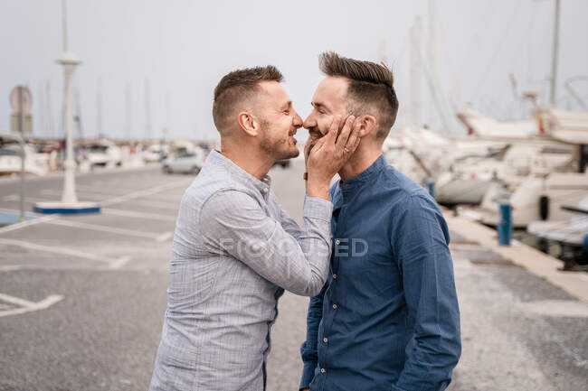 Homem feliz com corte de cabelo moderno rindo enquanto fala com parceiro homossexual na camisa durante o dia — Fotografia de Stock