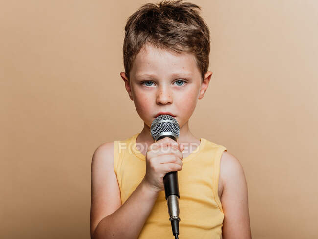 Criança legal em cantar no microfone moderno em fundo marrom no estúdio — Fotografia de Stock