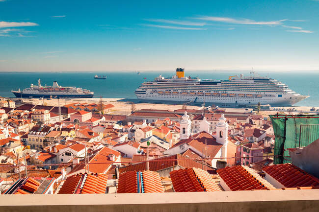 Barcos modernos amarrados en el puerto de cruceros de Lisboa cerca de casas con techos de tejas rojas contra el cielo azul en el día soleado en Portugal - foto de stock