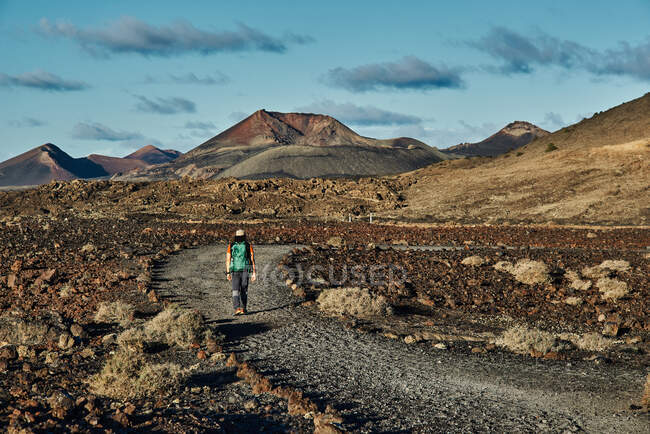 Caminhante anônimo com mochila andando no caminho seco no vale perto de colinas no dia nublado de verão em Fuerteventura, Espanha — Fotografia de Stock