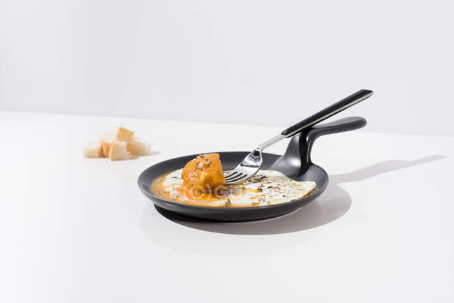 Кусочки хлеба подаются на белом столе с аппетитным жареным яйцом на сковороде с вилкой — стоковое фото