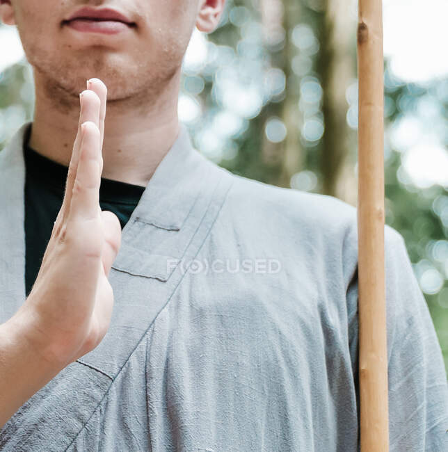 Обрізаний невпізнаваний чоловік з палицею тримає руку біля грудей, практикуючи кунг-фу в лісі — стокове фото