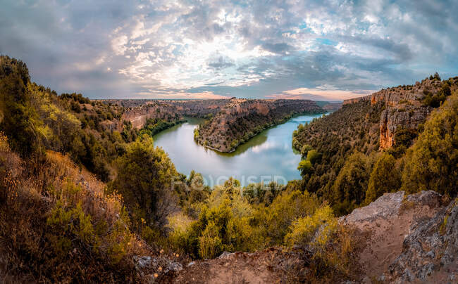 Vue panoramique des monts avec des arbres d'automne et la rivière sous un ciel brillant avec des nuages pelucheux au coucher du soleil en Espagne — Photo de stock