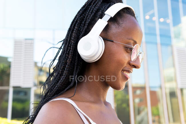 Positive African American female in headphones sitting in street in Barcelona and enjoying songs while looking away — Stock Photo