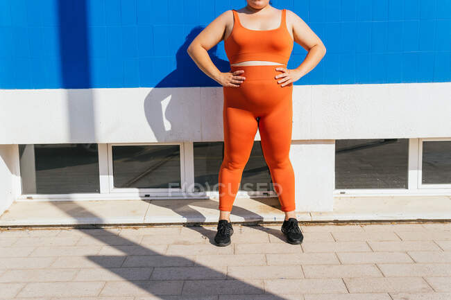 Atleta femenina anónima con sobrepeso en uso activo contra la pared de azulejos azules en un día soleado - foto de stock