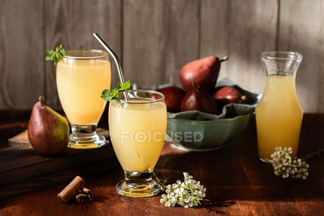 Copos de deliciosas bebidas refrescantes com suco de pêra e folhas de sabugueiro frescas na mesa com paus de canela — Fotografia de Stock