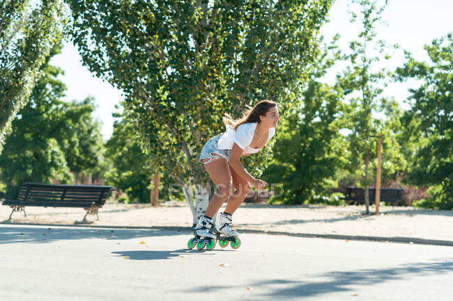 Вид збоку на жінку в роликових лопатях, що показують трюк на дорозі в місті влітку — стокове фото