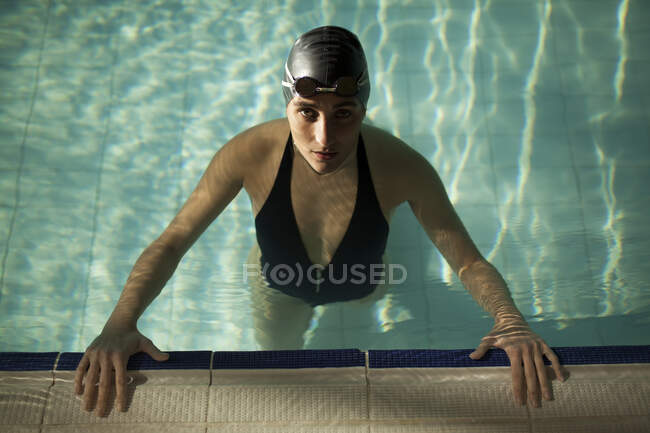 Mulher bonita jovem na piscina interior, vestindo maiô preto, olhar para a câmera — Fotografia de Stock