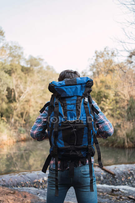 Escursionista maschio con zaino in piedi sul lago nel bosco e guardando altrove — Foto stock
